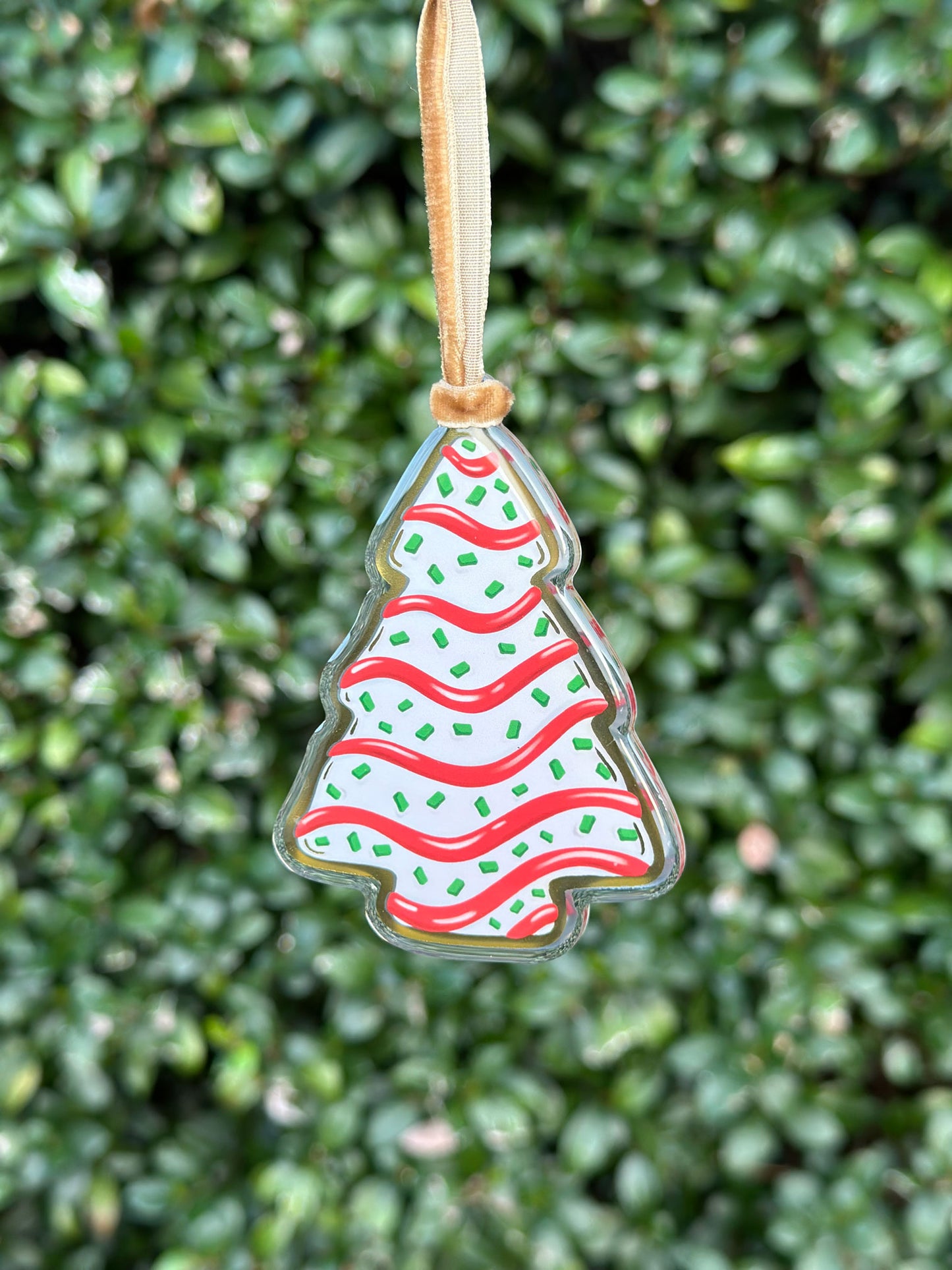 Christmas tree-shaped cake treat ornament with red and green design hanging from a velvet ribbon on a green leafy background