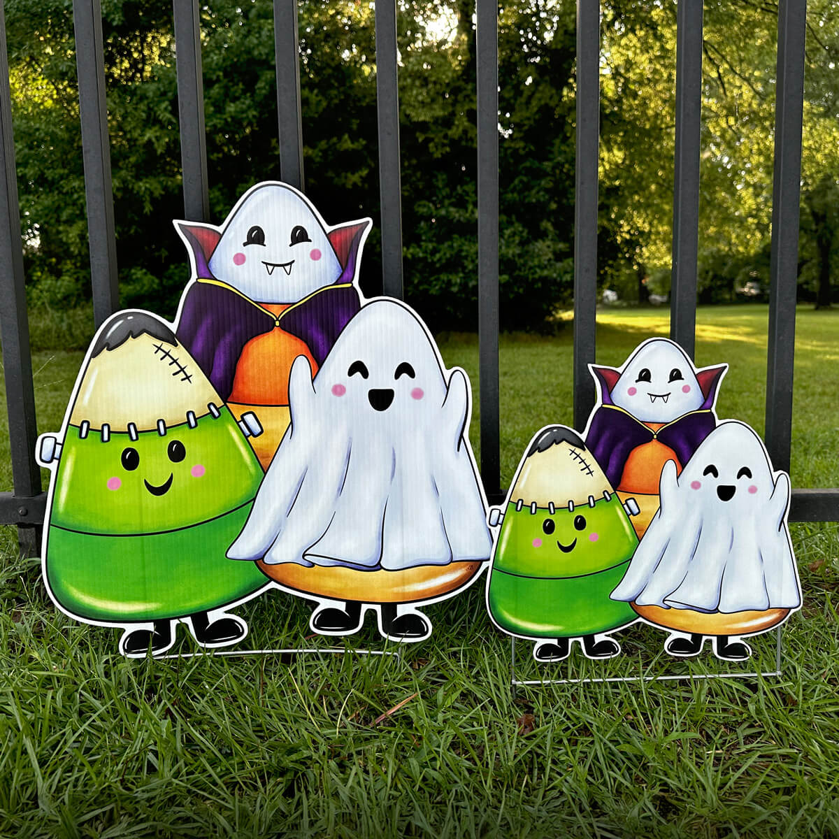 Halloween-themed candy corn corrugated yard sign decoration featuring a ghost, vampire, and monster in grass with a fence background.