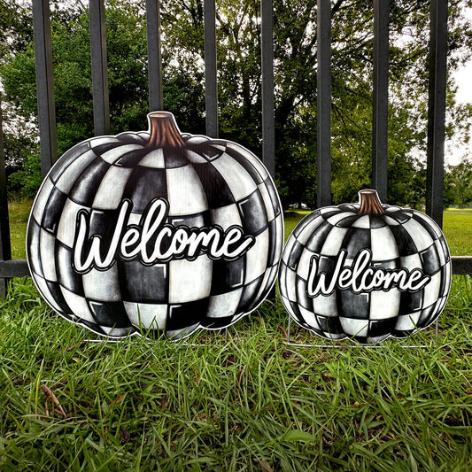 Two black and white checkered pumpkins with 'Welcome' text on a grassy background.