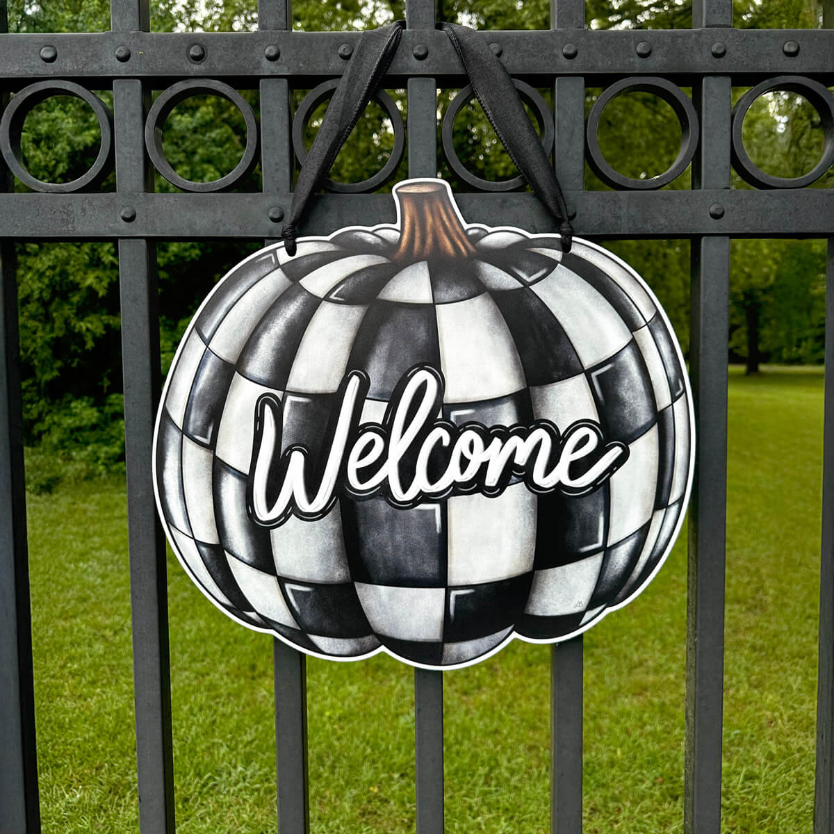 Decorative black and white checkered pumpkin door hanger with 'Welcome' text on a metal gate.