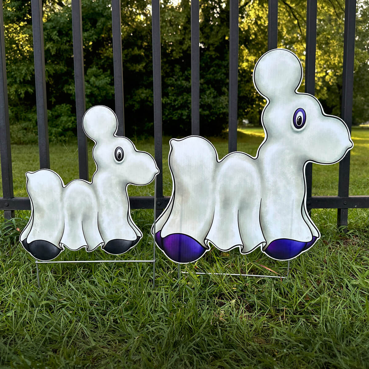 Two Ghost Bead Dog-shaped signs in purple and black colors on grass in front of a fence.