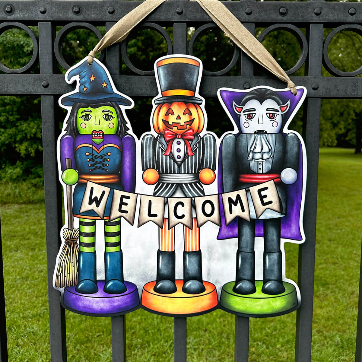 Decorative Halloween Nutcracker door hanger  featuring a witch, pumpkin, and vampire figure holding a 'Welcome' banner on a metal gate.