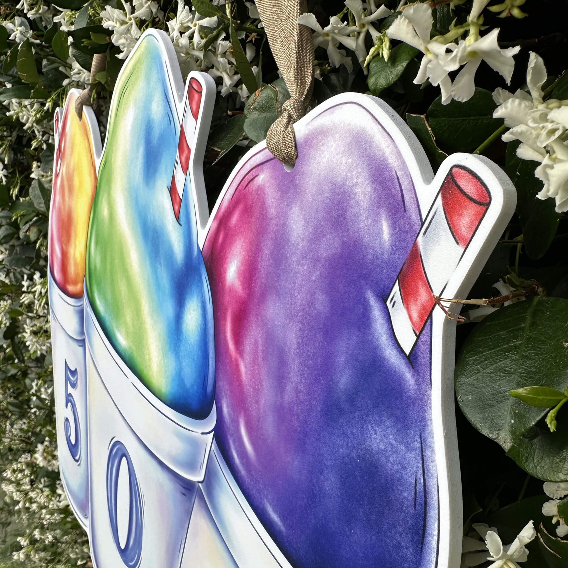 Colorful snoball door hanger close up with a red and white straw on a green leafy background.