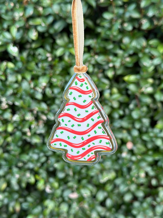 Christmas tree-shaped cake treat ornament with red and green design  hanging from a velvet ribbon on a green leafy background