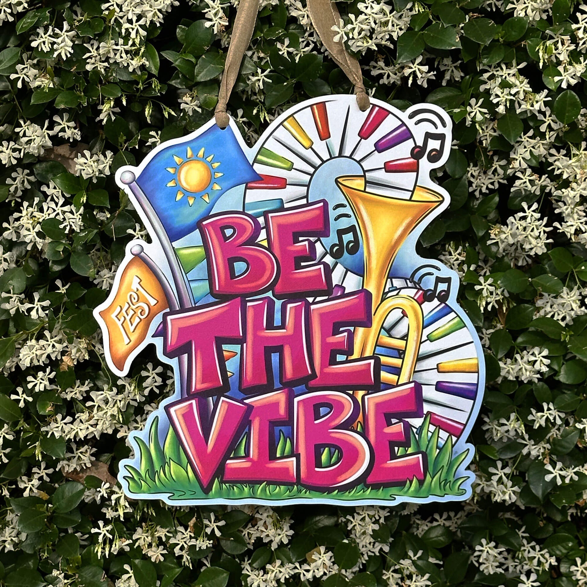 Decorative sign with 'Be the Vibe' text and musical elements, hanging against a green leafy background.
