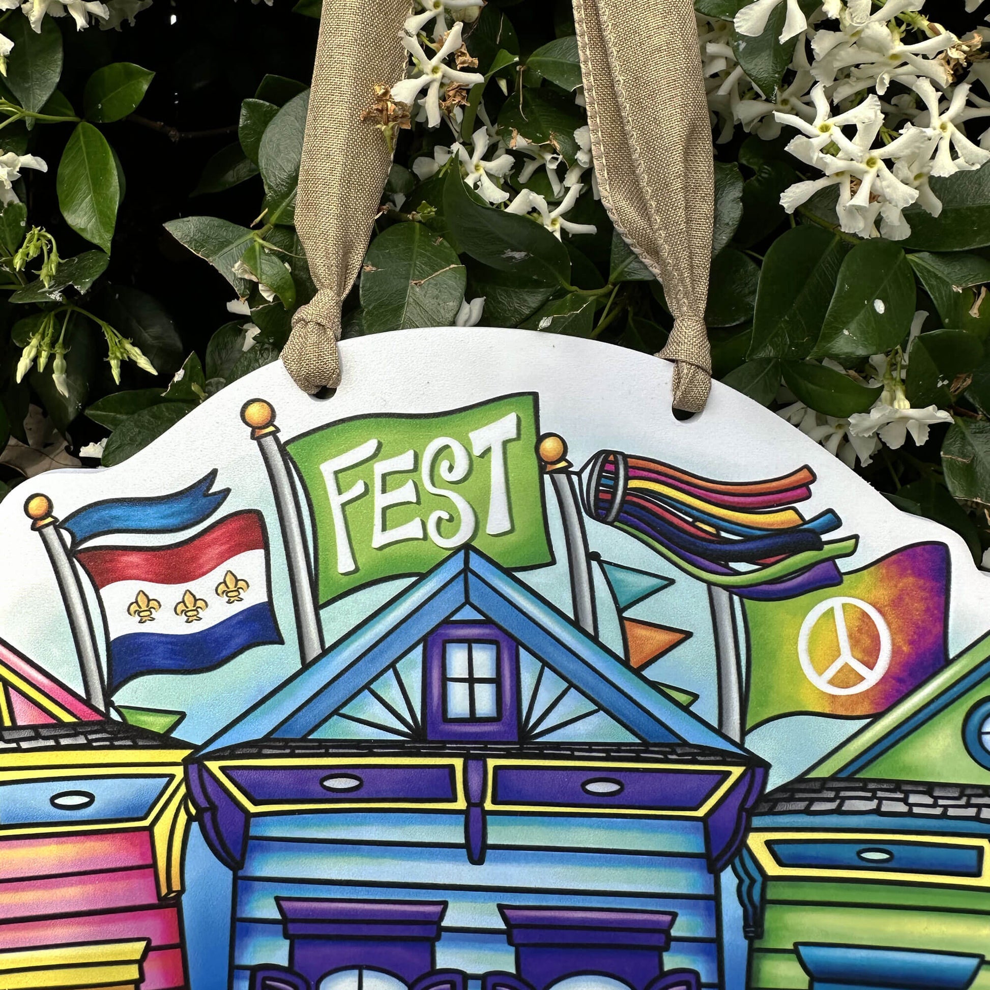 Colorful decorative shotgun sign with 'FEST' and various symbols hanging against a green leafy background.