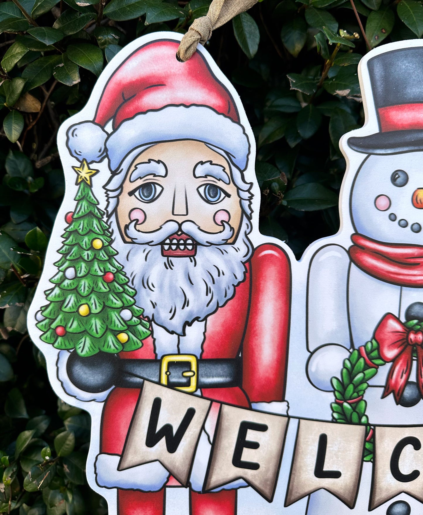 Decorative Christmas door decor detail of Santa Claus holding a tree and snowman against a green leafy background
