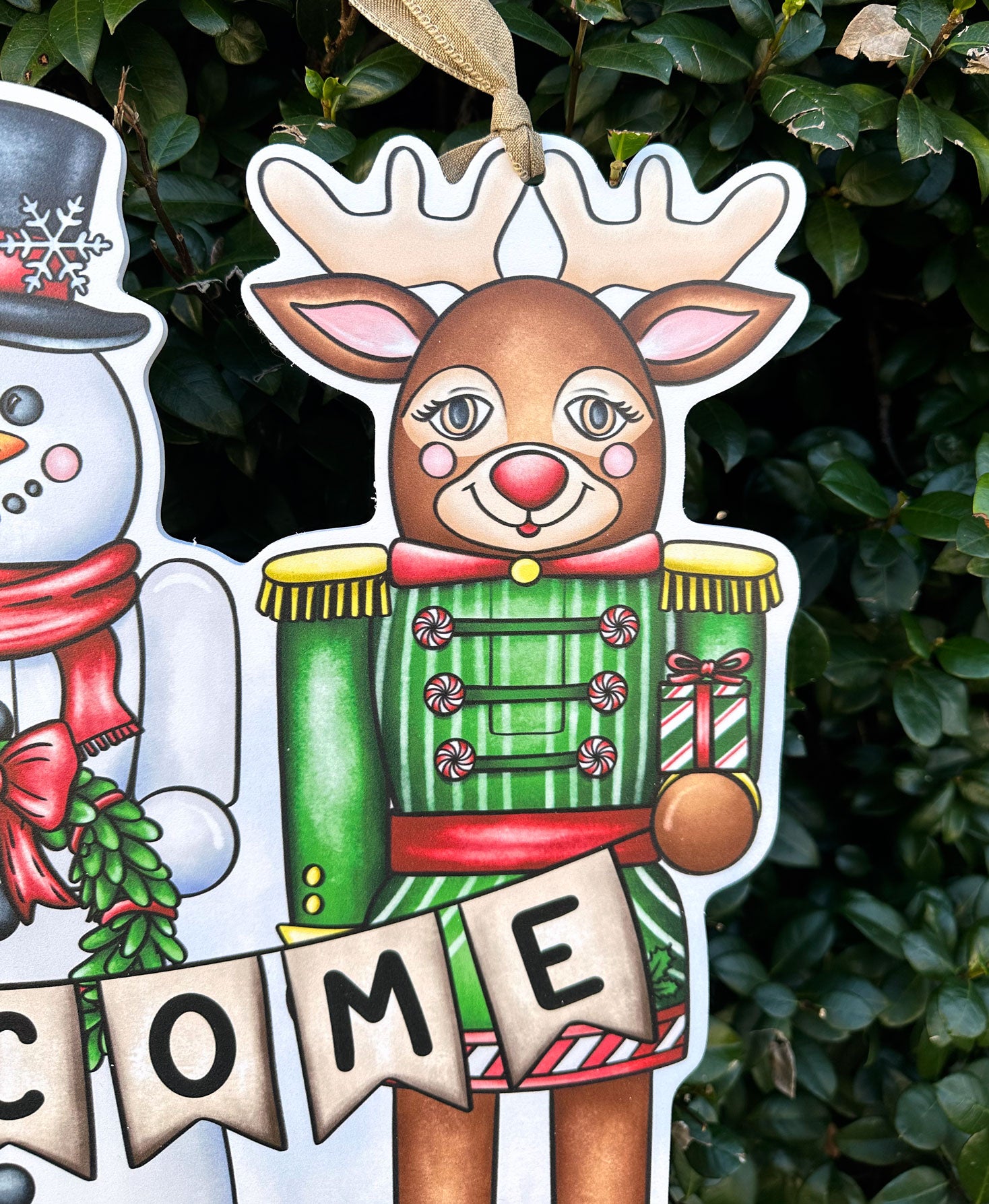 Decorative Christmas door decor detail of a reindeer holding a present and snowman on a green leafy background