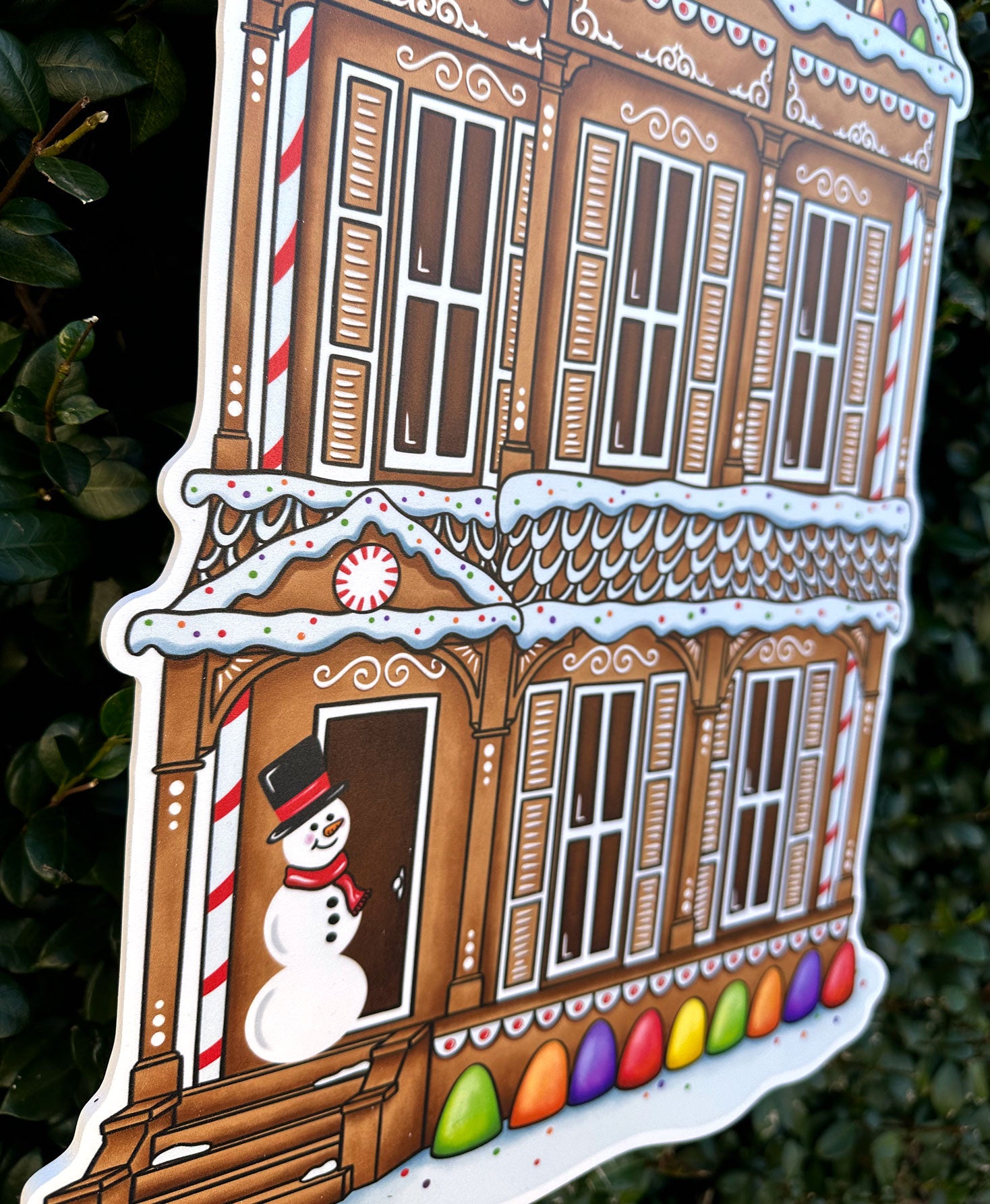 Decorative gingerbread shotgun house door decor with a snowman and candy decorations on a dark background