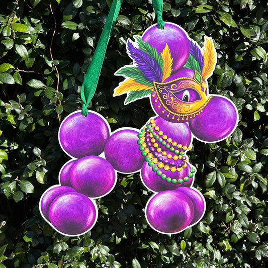 Decorative Mardi Gras door hanger of a bead dog with purple, green, and gold tones. Bead dog is wearing beads and a mask with features against a green leafy background.
