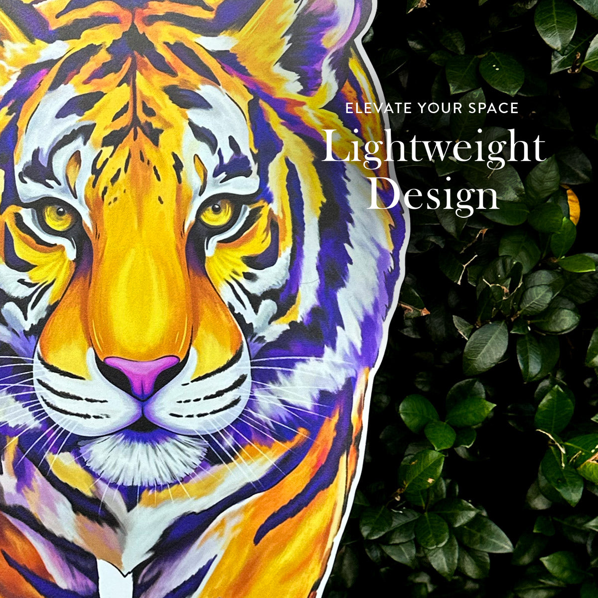 A large decorative front door hanger featuring a colorful hand illustrated tiger face in orange, yellow, white, and purple, shown against a background of dark green foliage. White text on the cushion reads 'ELEVATE YOUR SPACE Lightweight Design'.